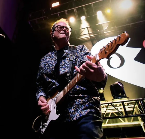 David Hunter playing electric guitar on stage, shot from below against the overhead lighting rig
